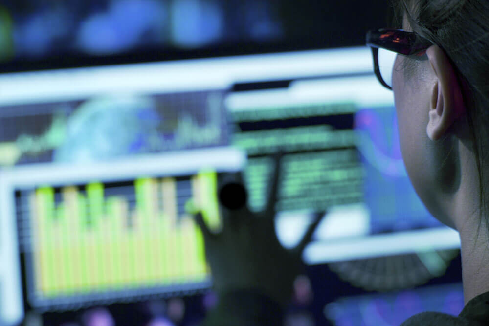 A student looks several different, colorful monitors, viewed from behind.