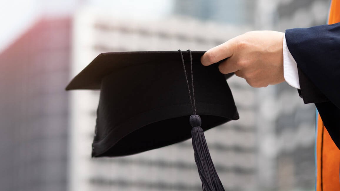 Close up of a hand holding a graduation cap.
