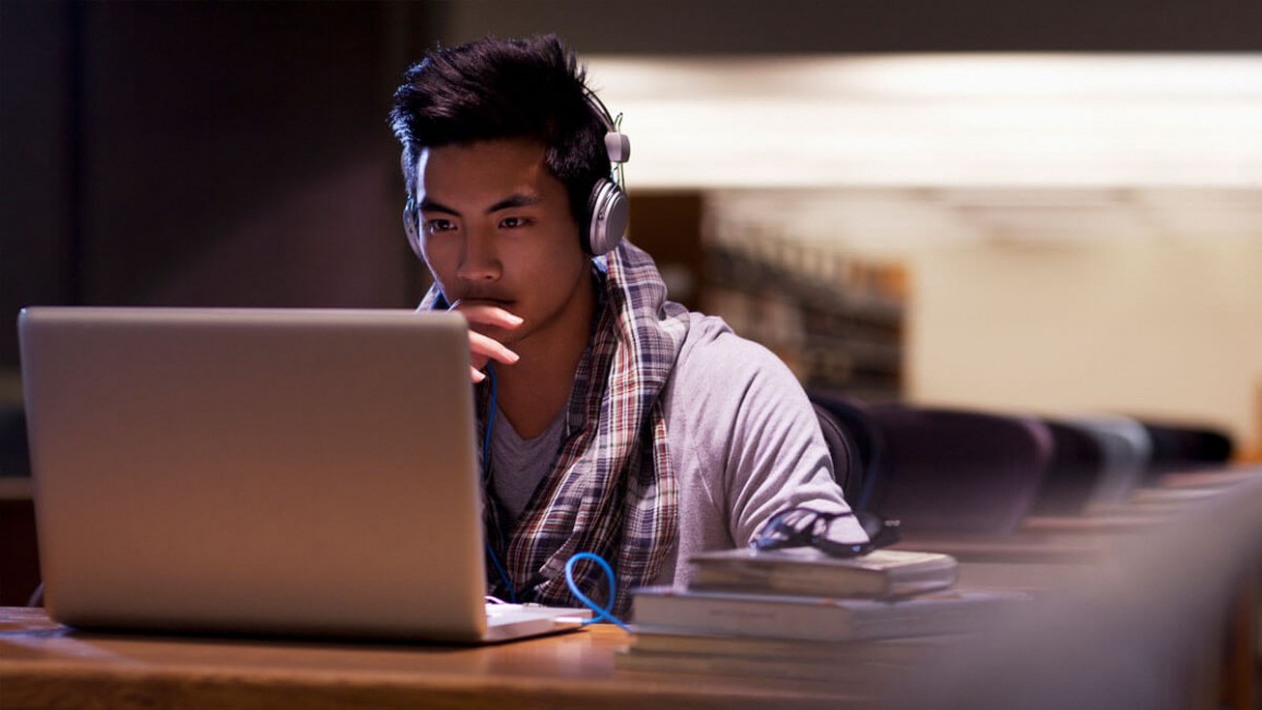 A student wearing headphones sits in front of his laptop.