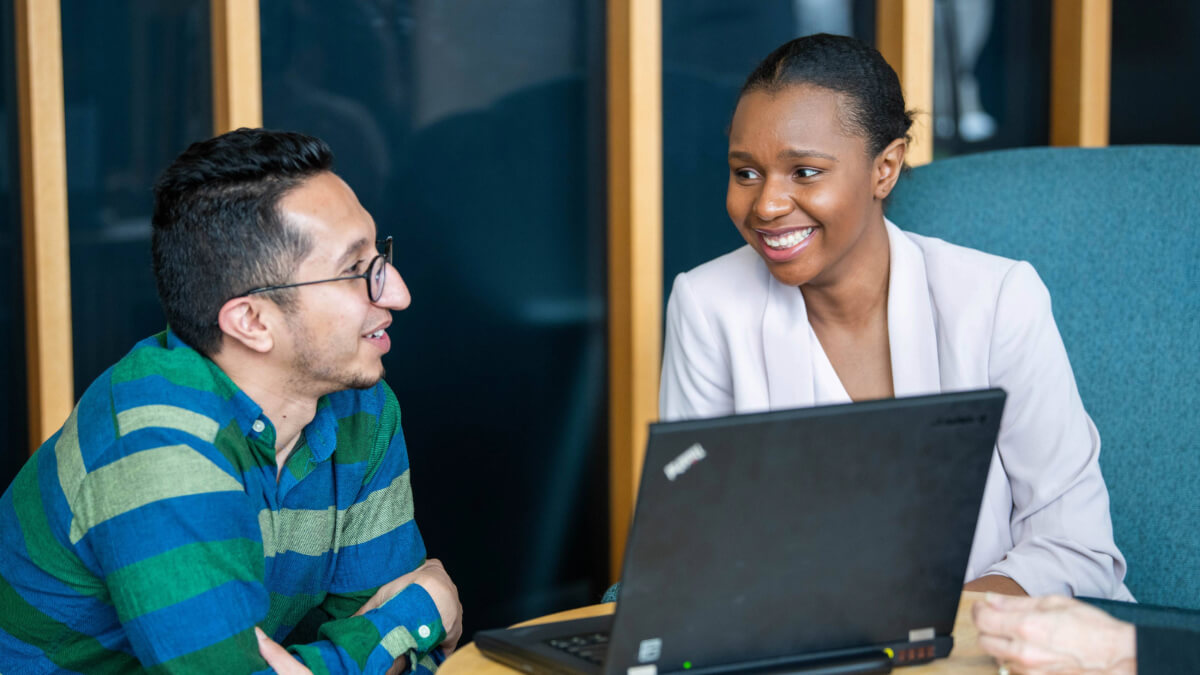 Two students smiling at eachother at a table in front of a laptop
