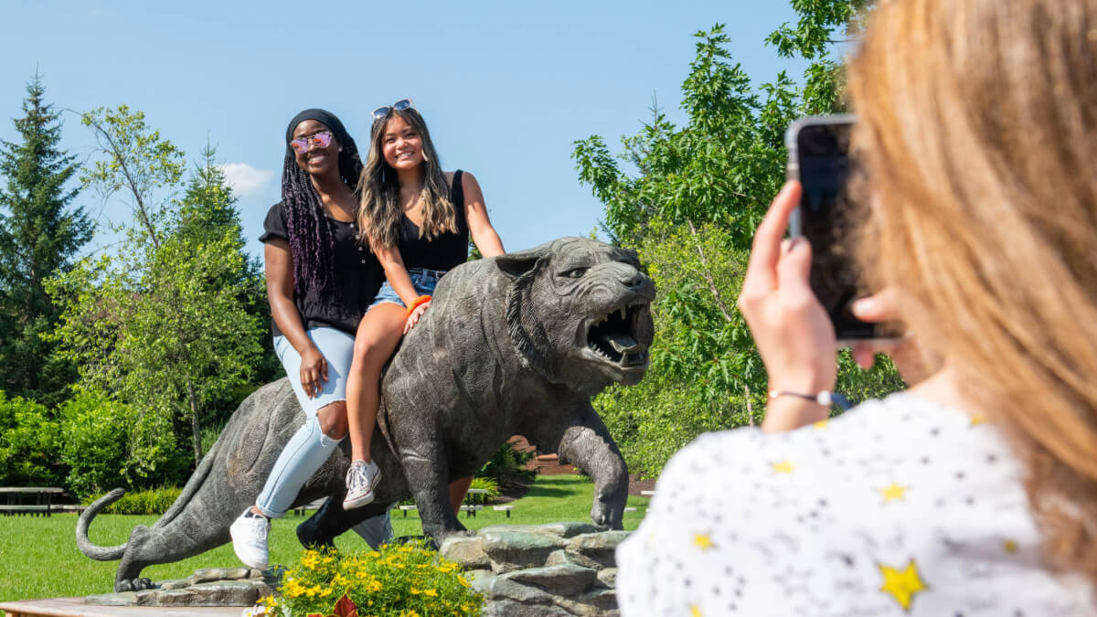 Students posing for a photo on the Tiger statue outside of RIT