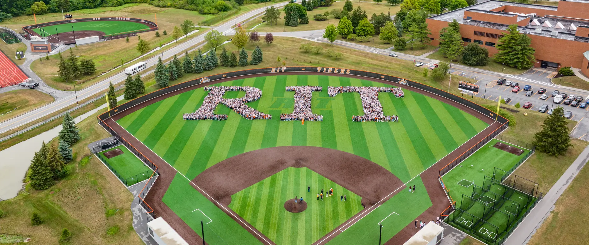 New students standing together on the baseball field making the letters RIT 