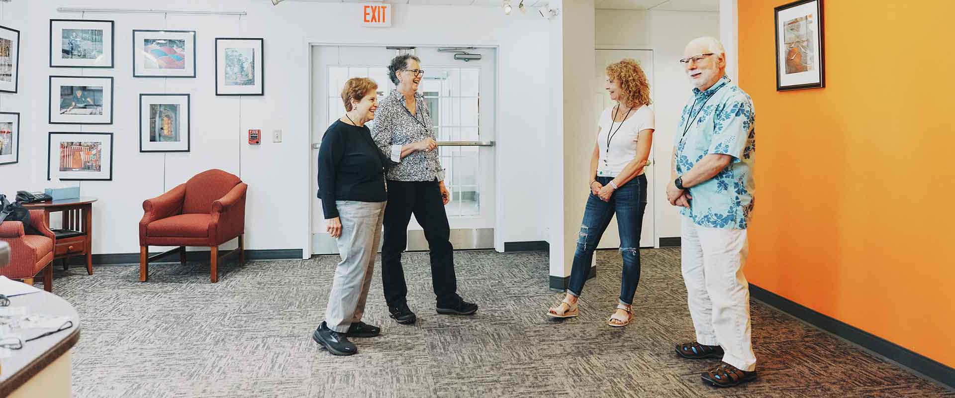 Four adults standing and talking in a brightly lit hallway with photo art on the walls.