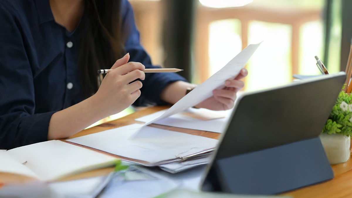 A closeup of a person sitting at a desk in front of papers and a laptop.