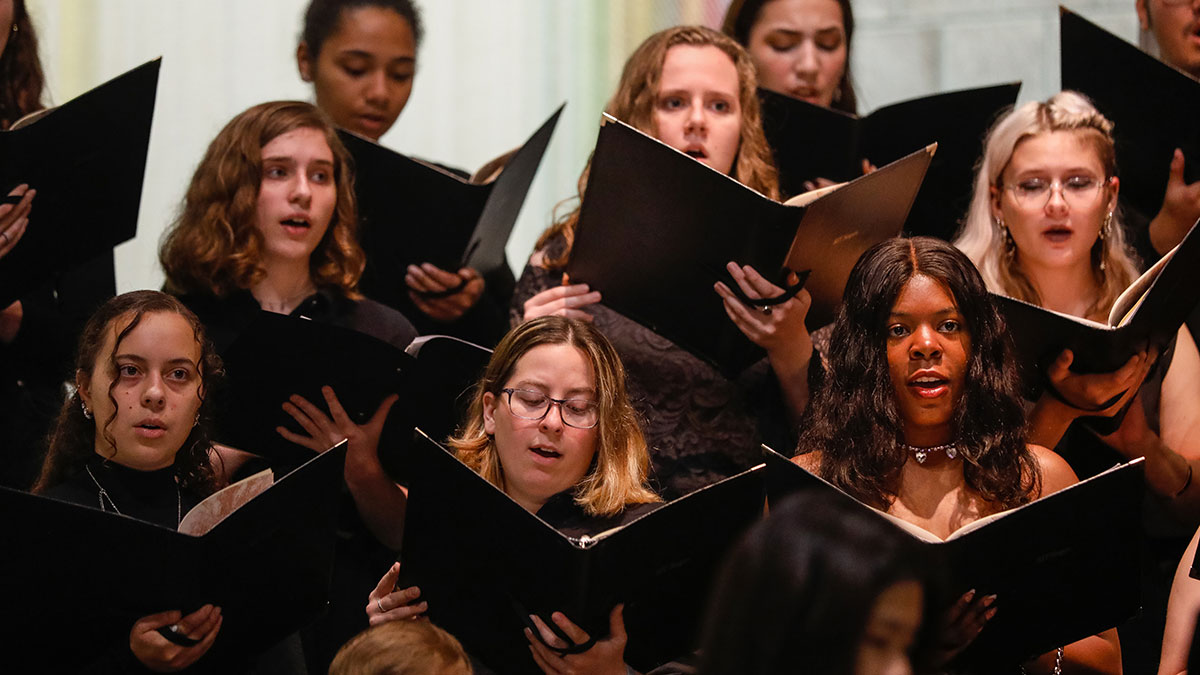 a group of students singing while looking at binders of sheet music.