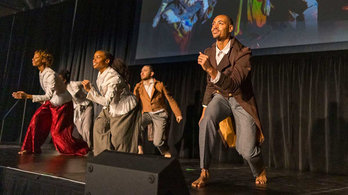 dancers wearing baggy period clothing dance on stage.