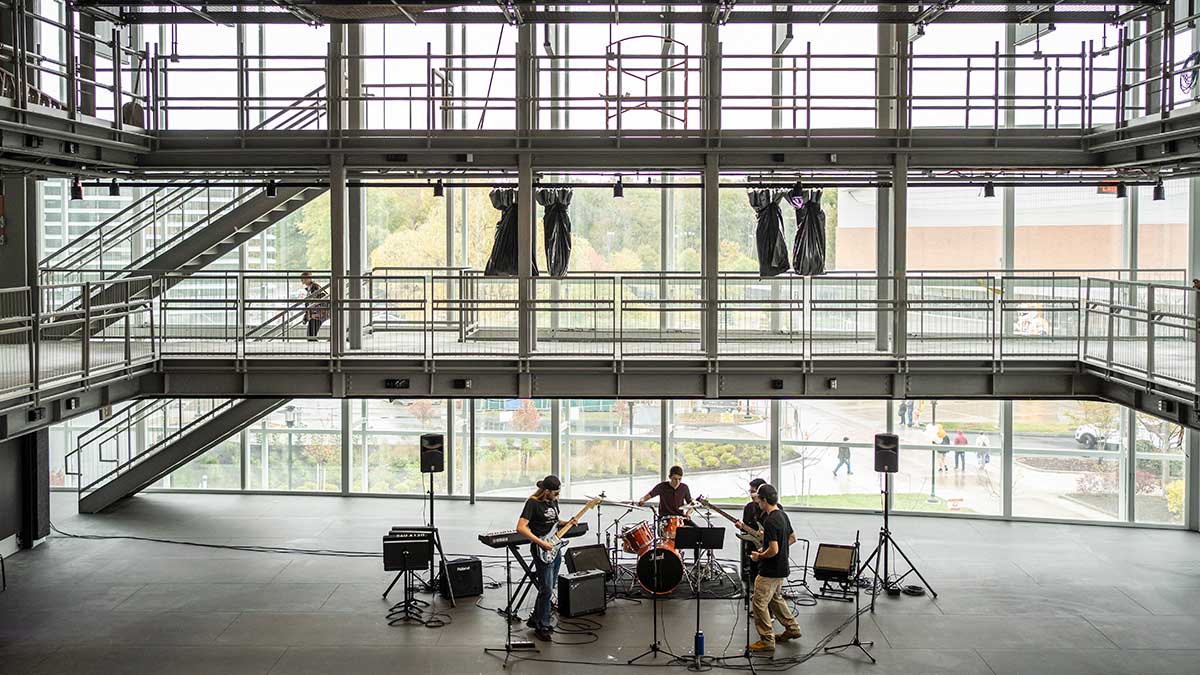 a small rock band playing on the lower level of an open, glass-walled, multistory space.