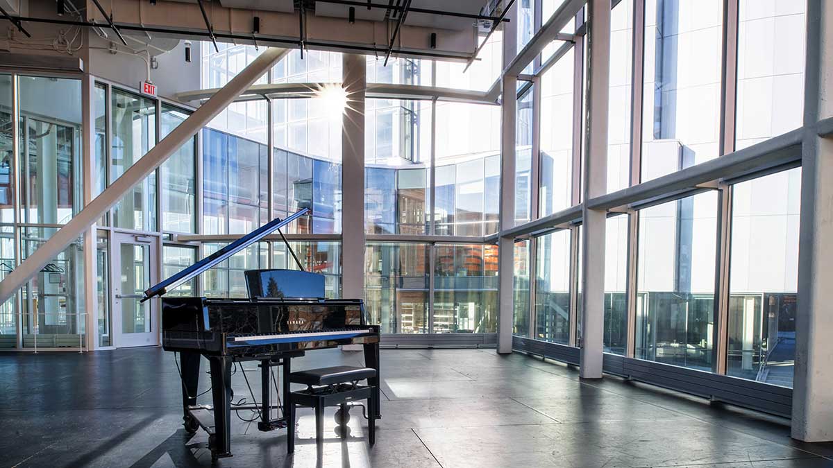 a large performance space with a piano and wall to ceiling windows.