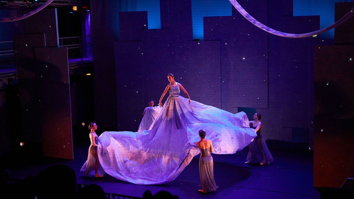a person on stage in a flowing dress being lifting into the air with a harness.
