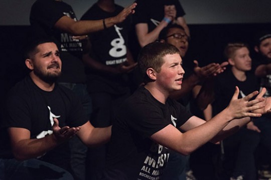 students in an a cappella group singing with their hands outstretched.