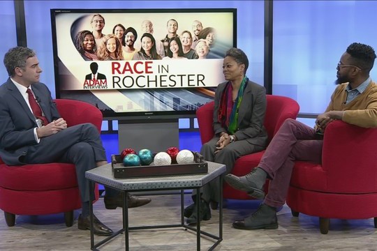 THree people sit in red chairs on set of TV news station
