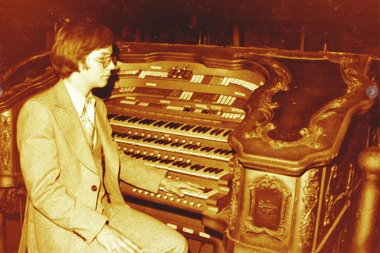 an amber colored photo shows an old organ and a man playing it.