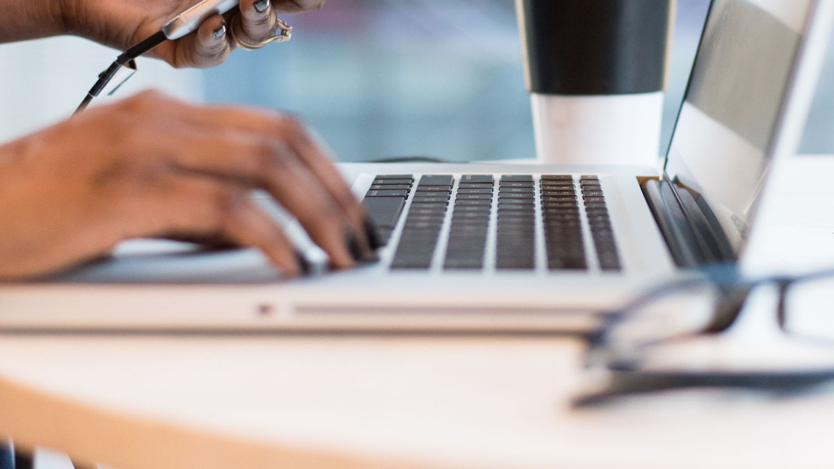  A person focused on typing on a laptop computer, with hands positioned on the keyboard and a screen illuminated.  