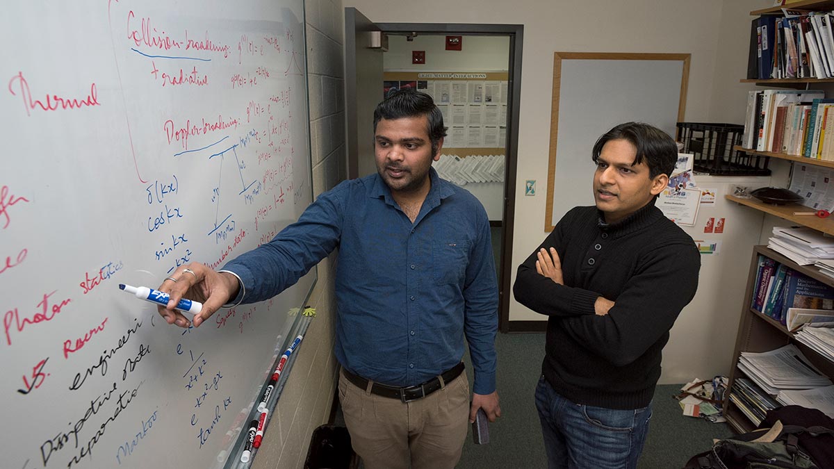 researcher pointing to a phrase on a whiteboard while a professor looks on.