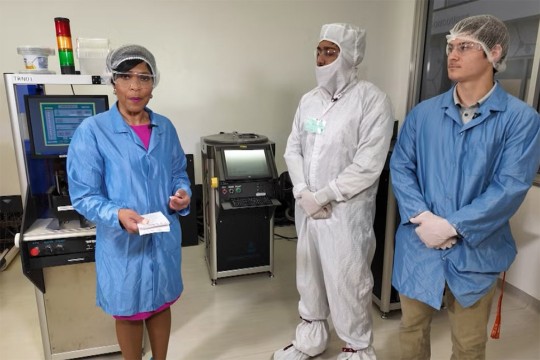 a woman in a blue medical suit stands next to two men in similar suits in a lab.
