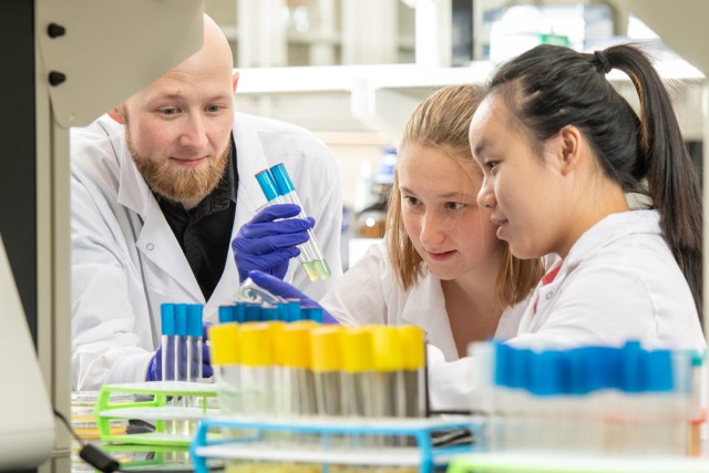 a man in a white lab coat assists two women in a lab.