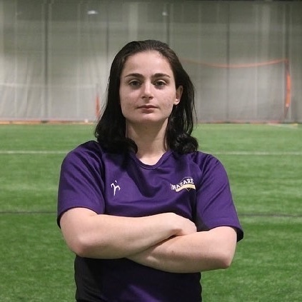 Leah poses with her arms crossed in front of a turf field.