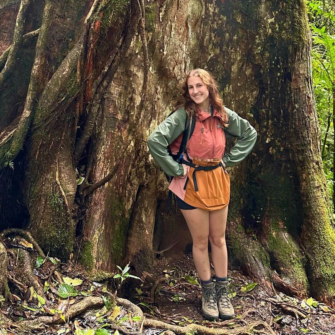 Autumn Potts standing at the base of a very large tree.