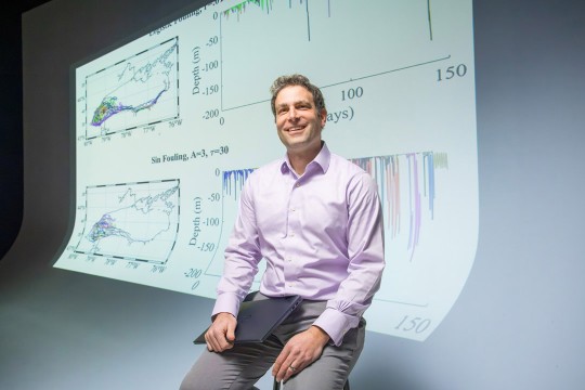 a man in a purple shirt sits in front of a screen showing data