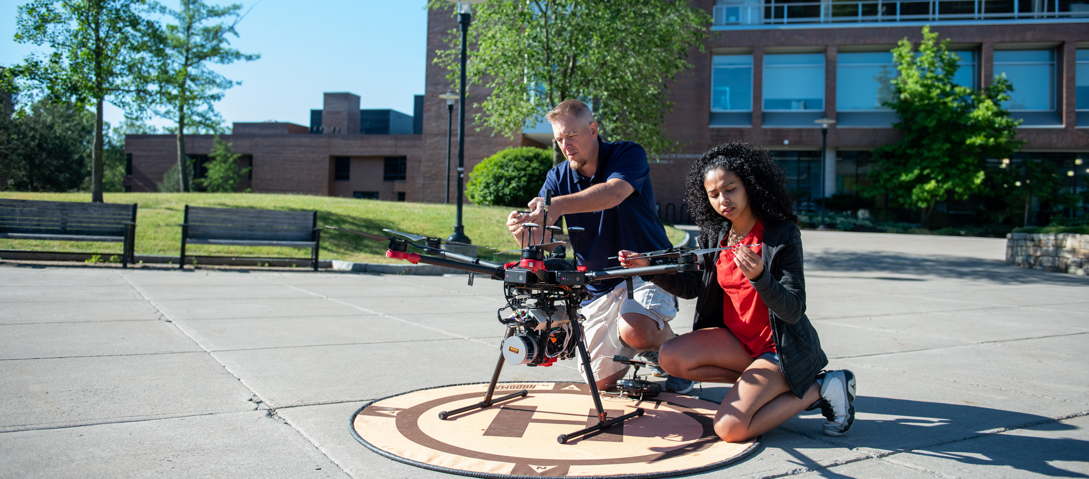 a student and teacher work on a drone in a quad
