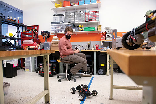 Students working in a workshop with a remote control car on the floor.
