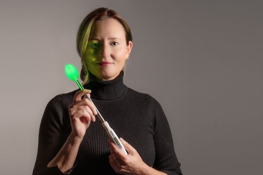 woman holding a medical wand with a glowing green bulb on the end.