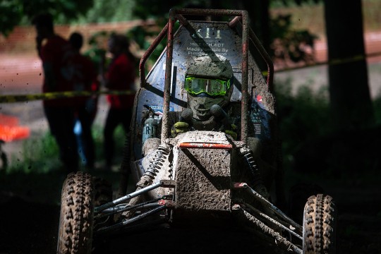 Head-on view of baja car and driver covered in mud.'