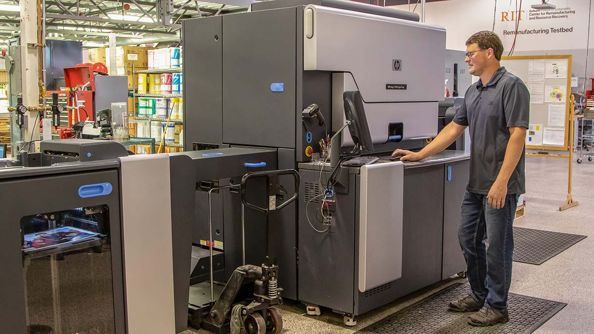 researcher standing next to a large, boxy piece of equipment that looks like an office printer.