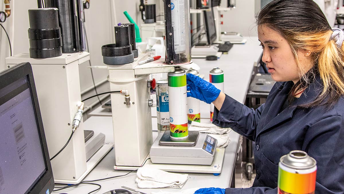 a lab worker looking at a computer while using a device to measure an ink canister.