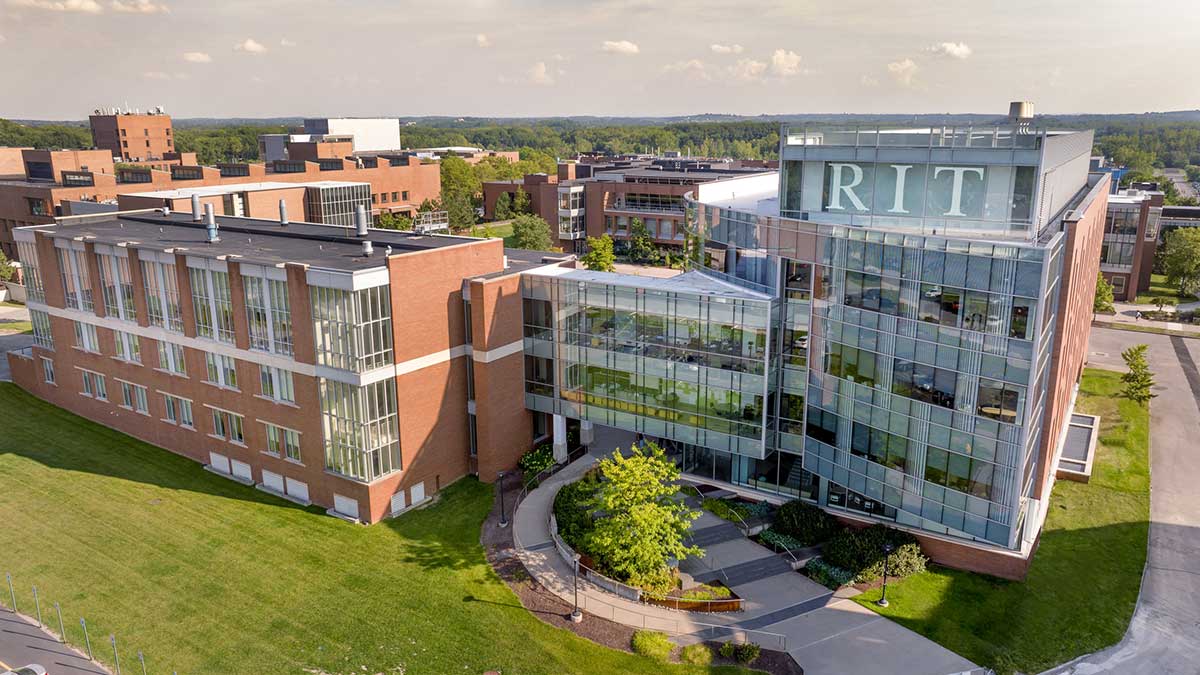 Aerial view of a modern RIT academic building with glass and brick architecture surrounded by greenery.