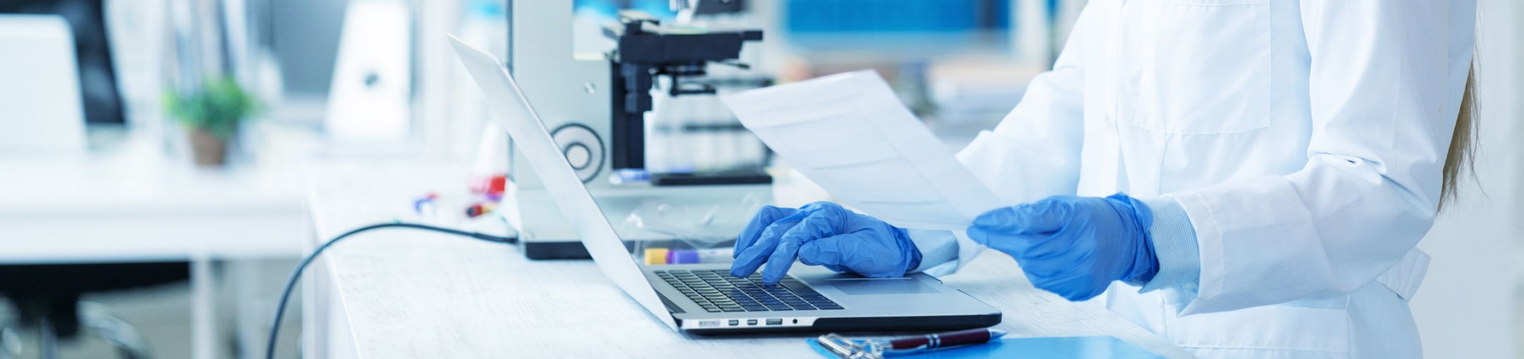 a person wearing glove and a lab coat using a computer and microscope