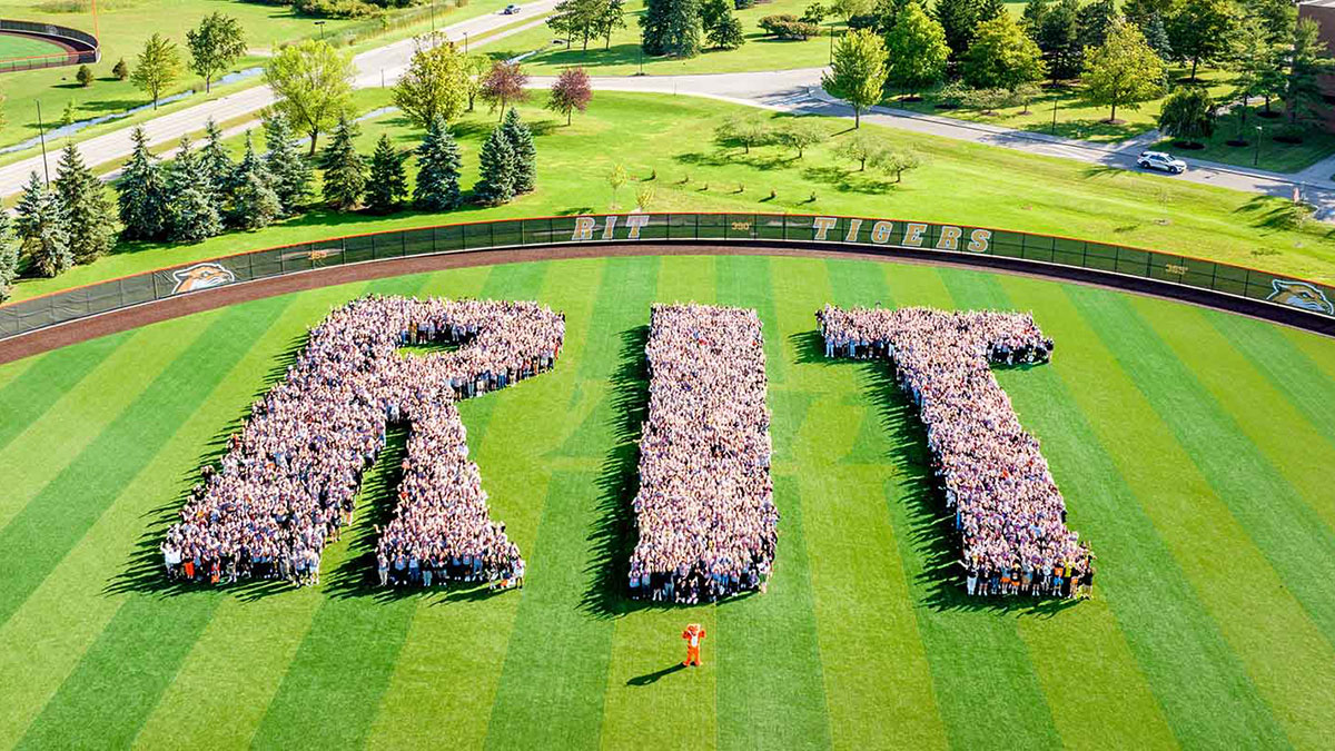aerial view of the outfield of a baseball field, with hundreds of students gathered to form the shape of the letters R I T.