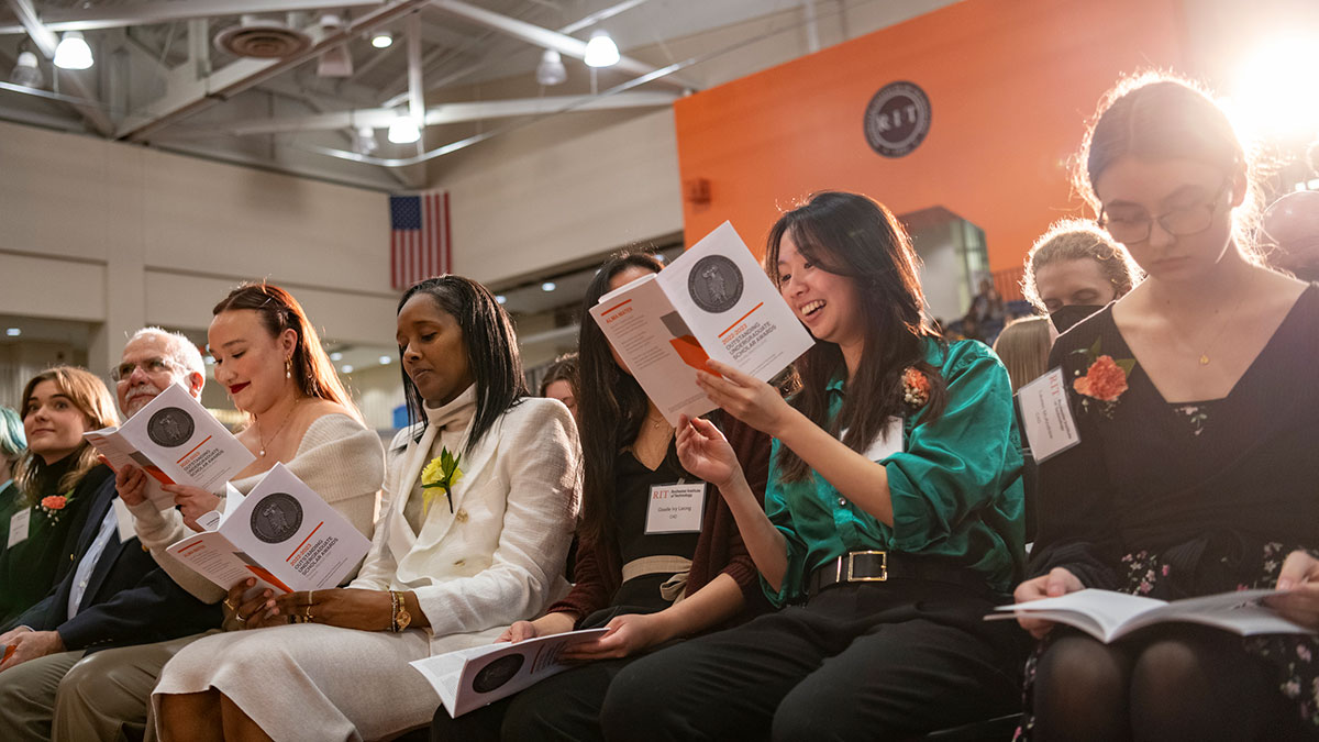 A close-up of seated attendees reading programs and smiling during an awards ceremony.