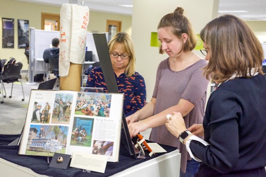 Jody Sidlauskas, Taylor Carpenter, and Juilee Decker work together to place artifacts into a display case in the library.