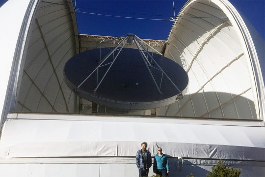 Researchers stand in front of gigantic observatory.