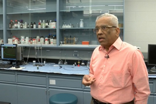 professor talking in front of cabinet full of various sized bottles.