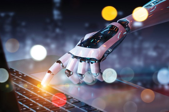 a robotic hand with the pointer finger outstretched to click the spacebar on a laptop.