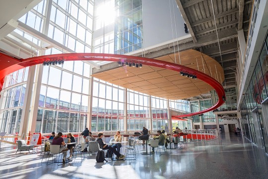 interior view of a large open study space with glass walls and a round red structure suspending light fixtures.