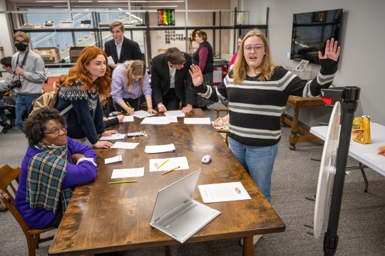 five people crowded around a table as another spins a prize wheel.