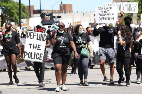 crowd of protestors walking down a street with signs that read, defund the police, and skin color is not reasonable suspicion.