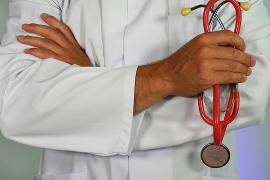 the torso of a doctor appears in a lab coat holding a red stethoscope