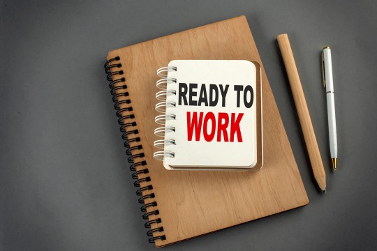 a stock image of business supplies on a gray background including a notebook that says Ready to Work.