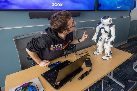 Man in NASA sweatshirt works on a two-foot-tall white robot.