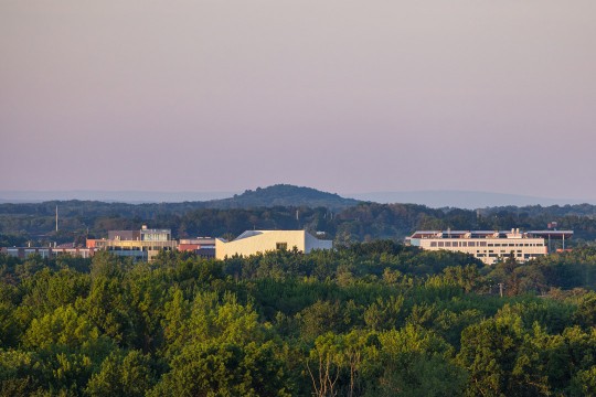 The tops of buildings on the R I T campus appear during sunrise behind trees.
