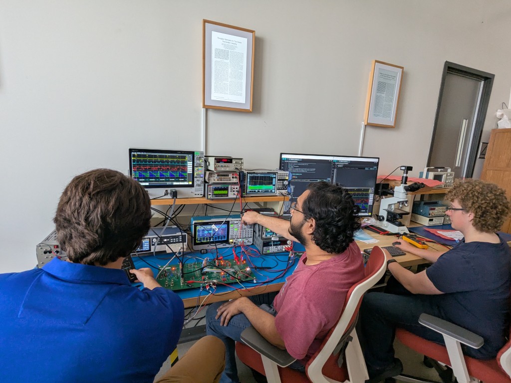 Three students working at the RAMLab high frequency validation bench, surrounded by oscilloscopes and signal generators
