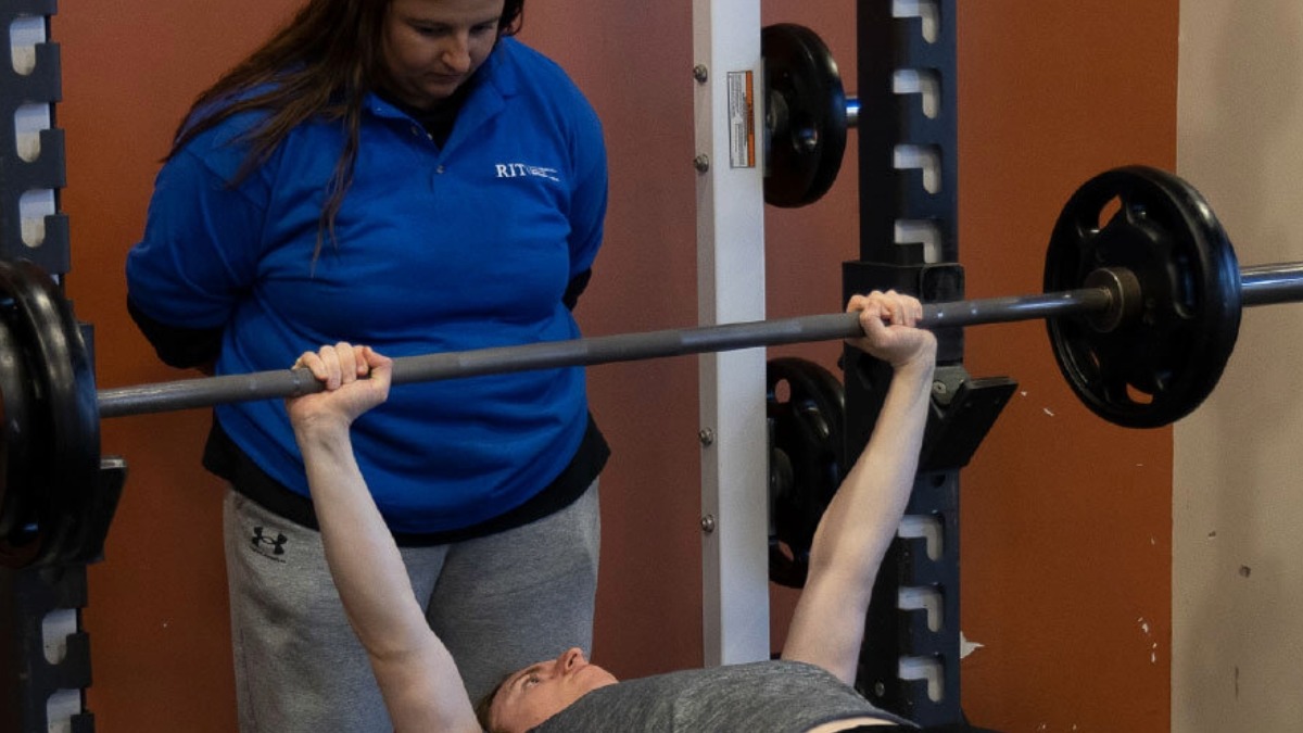 One student employee spotting another student bench pressing weights.