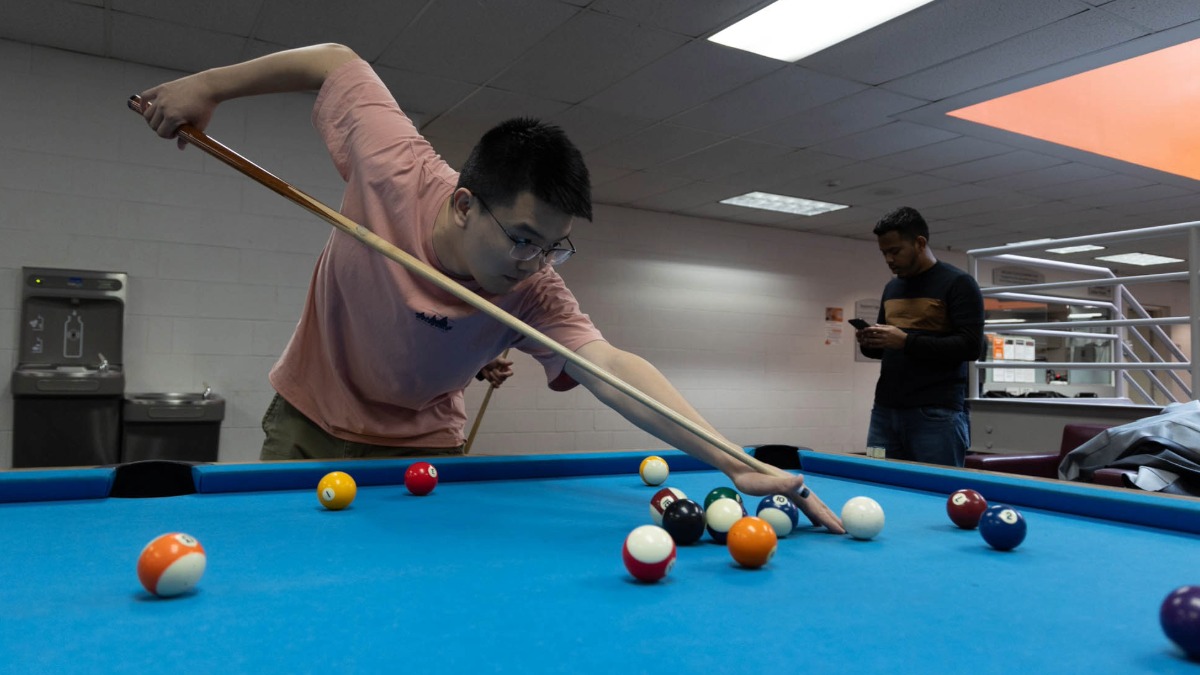 A student taking a shot during a game of billards on a blue pool table 