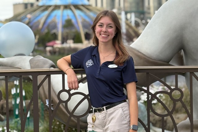 a college age woman in khaki pants and a blue polo shirt leans against a metal railing at Universal Studios Orlando