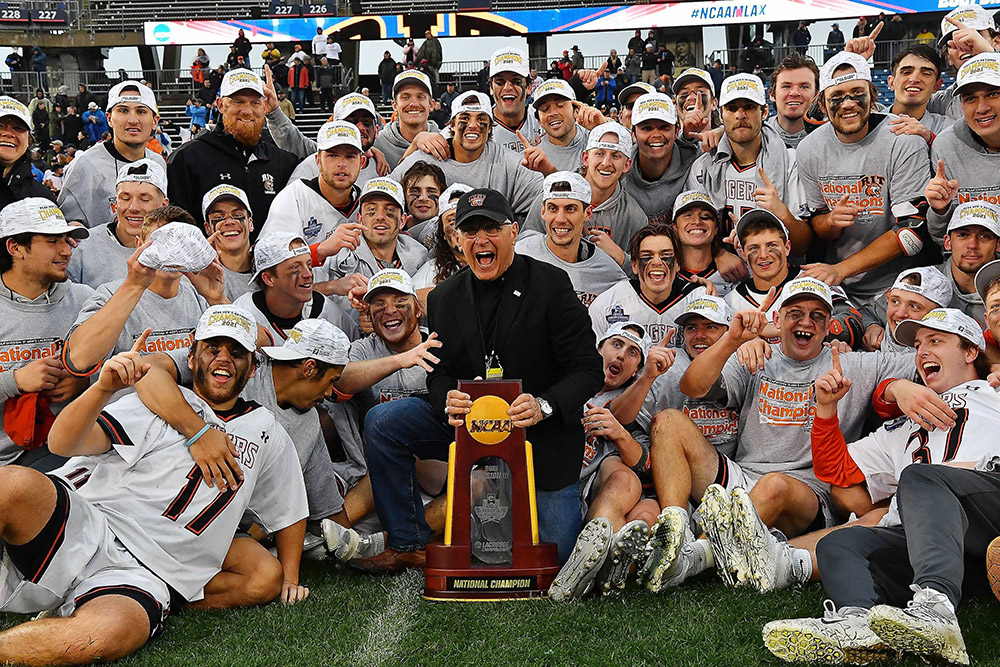 athletics director with championship trophy surrounded by team members.