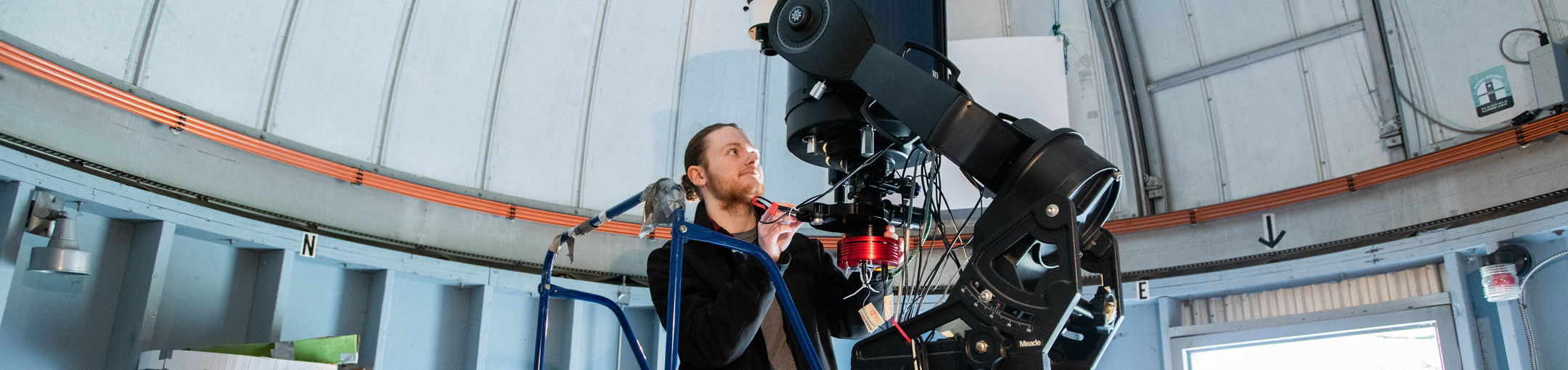 male student behind telescope in observatory